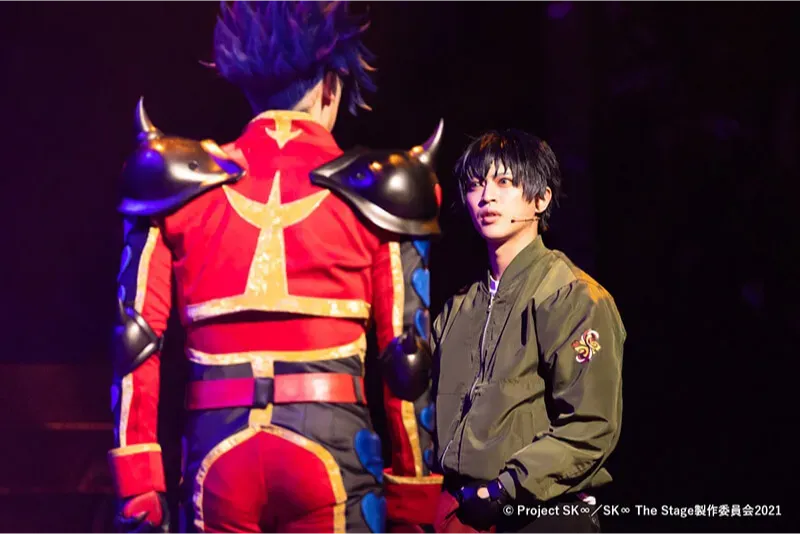 Mashu Ishiwatari as Snake talks to Adam on stage. Adam is facing away from the audience.